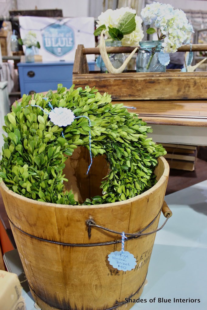 Preserved Boxwood wreath inside a wooden bucket with wooden tray and antlers in the background.