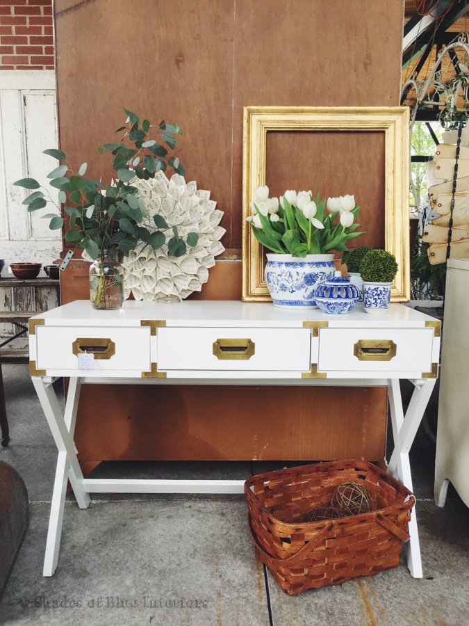 White campaign desk staged with flowers, gold frame, and sheet music wreath.