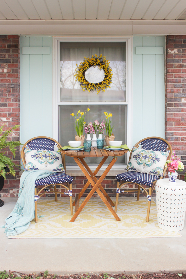 Spring front porch with bistro table and chairs, flowers, and forsythia wreath