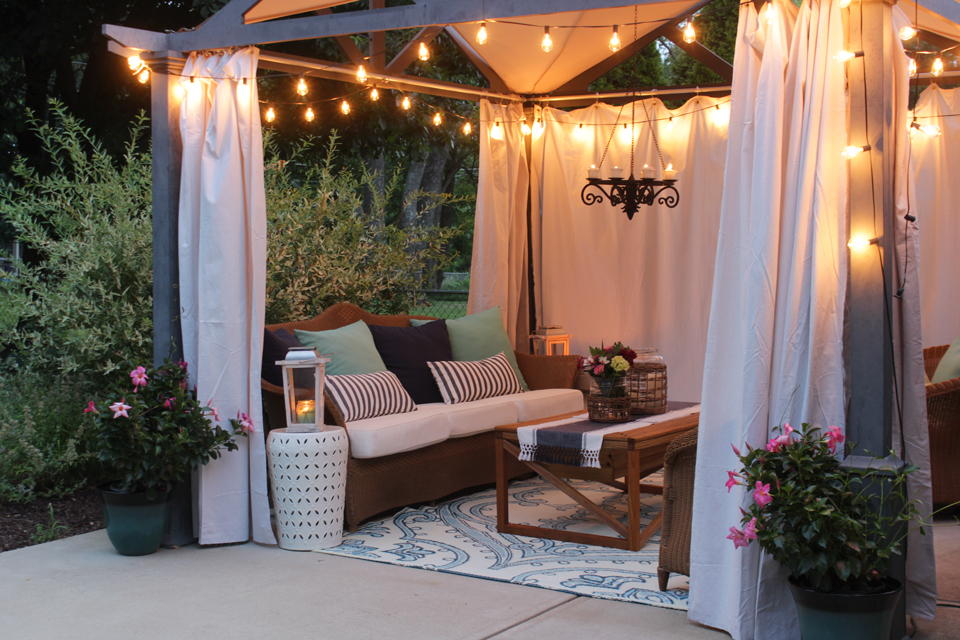 Pergola with edison bulb lights, canvas curtains and cozy seating at dusk