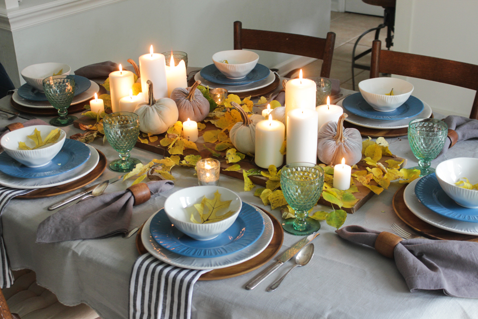 Fall tablescape with pillar candles, pumpkins, fall leaves, and layered place setting