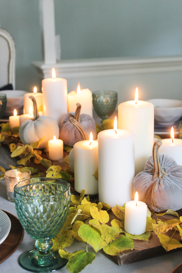 Fall centerpiece with lit pillar candles, velvet pumpkins on a bed of yellow leaves