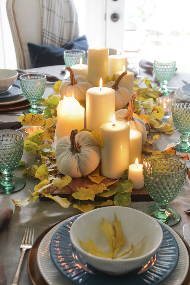 Lit pillar candles in a fall tablescape with fresh cut yellow leaves