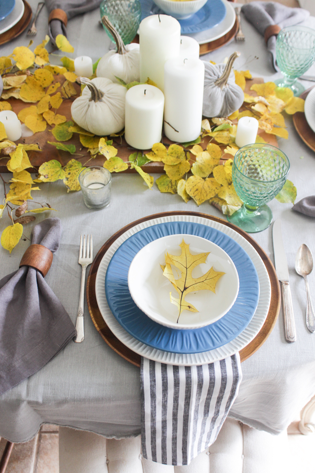Fall table with yellow leaves, natural wood accents, blue and white plates, green goblets