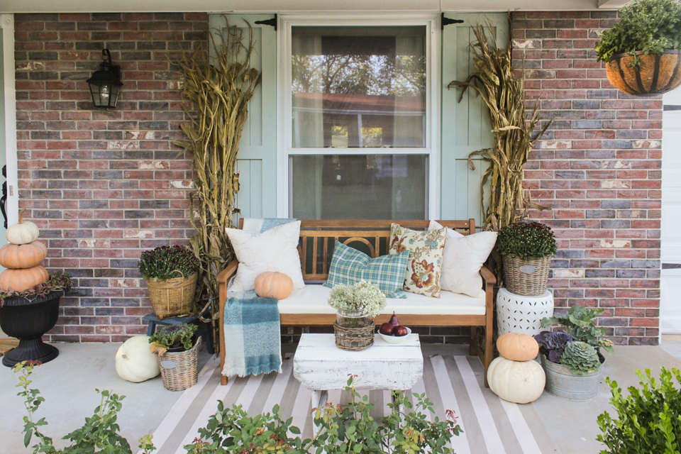 Fall front porch with wooden bench, pillows, cornstalks, and pumpkin topiaries