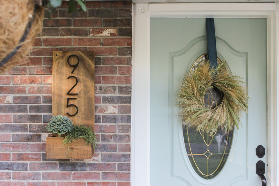 Wheat wreath on an aqua front door, and a wooden number sign with planter