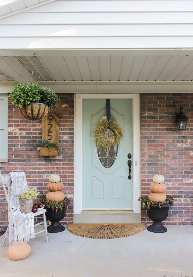 Fall front porch with pumpkin topiaries, wheat wreath, and wooden chair with throw
