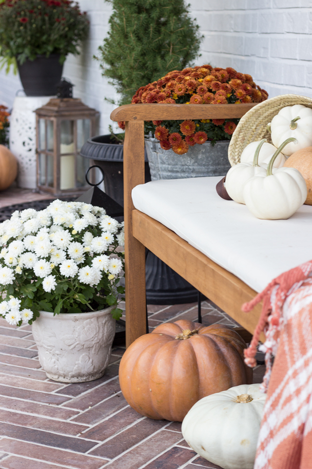 Pumpkins and mums surround a wooden bench on fall front porch