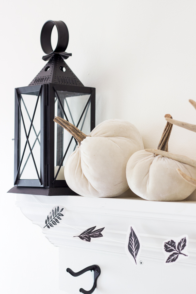 Black lantern, velvet white pumpkins, and leaf garland on fall mantel 