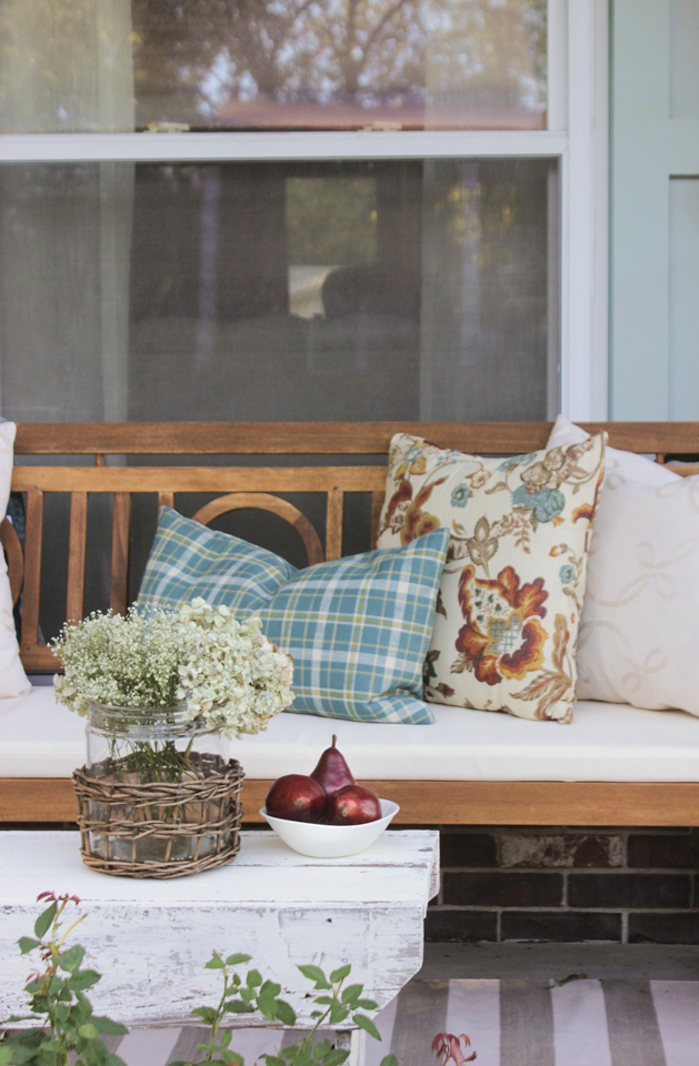 Fall front porch with wooden bench, pillows, cornstalks, and pumpkin topiary