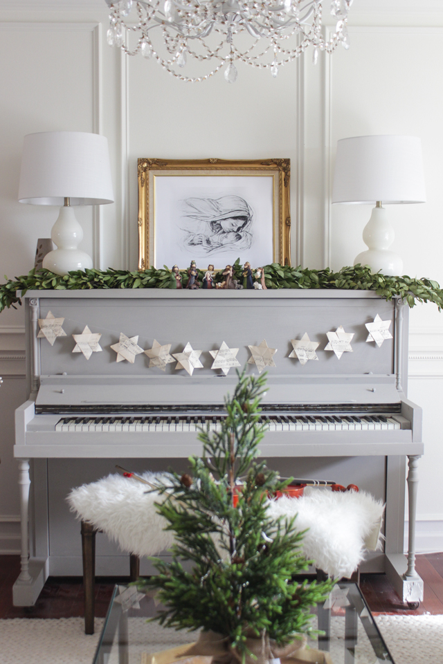 Gray piano, star garland, and framed Nativity pencil drawing on top